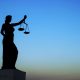 Blindfolded Lady Justice holding scales silhouetted against a dark sky
